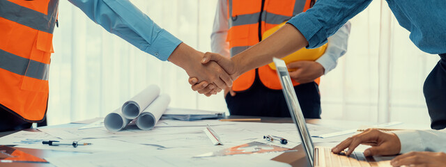 Construction engineer handshake with businessman contractor over architecture design blueprint on meeting table. Architect and engineer shake hand after successful cooperation teamwork. Insight