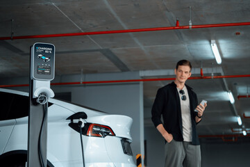 Young man travel with EV electric car to shopping center parking lot charging in downtown city...