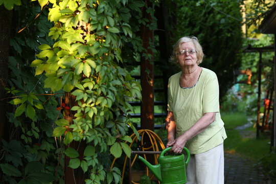 pensioner blond woman with water can on beautiful garden background closeup photo