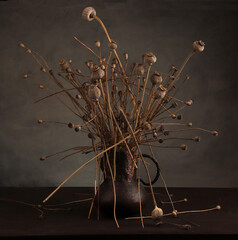 Abstract chaotic still life with dried poppy bunch in old cracked brass jug vase.  Composition of dried flowers poppies on dark background.