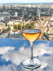 Glass of chilled rose wine on a table in a restauarnt overlooking a city. The sky and clouds are reflected in the table top.No people.