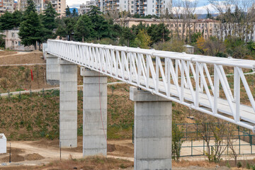 Iron pedestrian bridge over a small canyon painted in white. Tbilisi