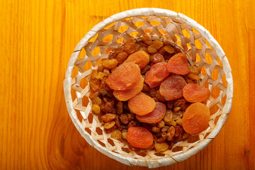 Dried apricots and raisins in a wicker plate on a wooden table