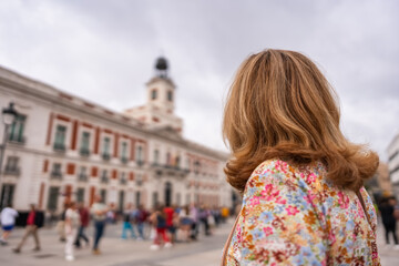 Tourist woman with her back looking at the clock tower of the Puerta del Sol buildings in Madrid.