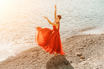 Woman red dress sea. Female dancer in a long red dress posing on a beach with rocks on sunny day. Girl on the nature on blue sky background.