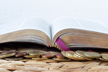 Coins money in front of open holy bible book with white background. Close-up. Copy space. Selective...