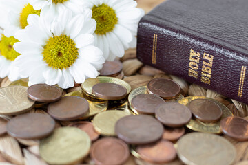 Coins, flowers, and holy bible book on rustic table. Close-up. Selective focus. Christian tithe,...