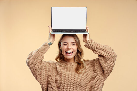 Happy student winks, holding laptop  on head showing computer screen, learning language, mockup. Smiling beautiful woman shopping online with sales isolated on background. Technology concept