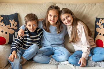 Small Group of Three Happy and Smiling Children at Home on the Sofa. Concept of Happy Siblings at Home at Christmas.