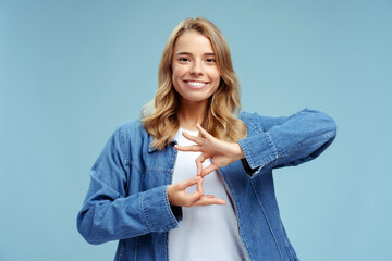 Smiling confident sign language interpreter or teacher communicating by hands gestures isolated on blue background. Nonverbal communication concept - obrazy, fototapety, plakaty