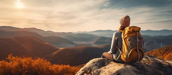 Fotobehang Back view young woman wearing a backpack and sit on stone in mountain at sunset © orendesain99
