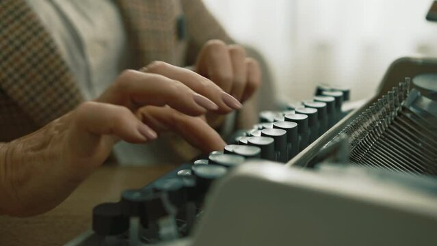 Nice well-groomed hands of lady in checkered jacket and white T-shirt working on vintage mechanical typewriter, sitting at table at daytime. Manual typing. High quality 4k footage