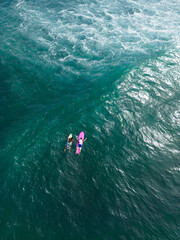 Aerial of two surfers paddling on boards over turquoise ocean waters, marine adventure and water sports from above. Athletes prepare to ride the waves. Freedom of the sea.