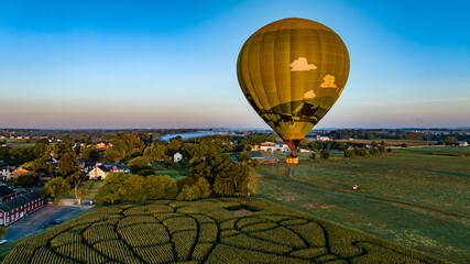 An Aerial View of a Golden Hot Air Balloon, Just Launched and Floating Across a Field With a Corn...