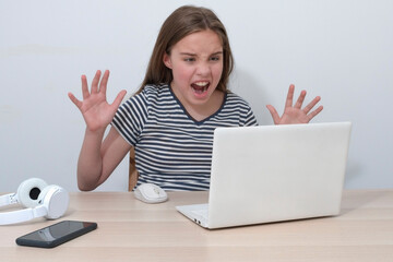 A teenage girl with a computer is angry with an interlocutor online. Non-working laptop. Striped t-shirt, negative mood