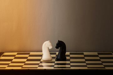 Two chess knights, one white and one black, stand facing each other on a chessboard. The confrontation of two opposites, the struggle between black and white