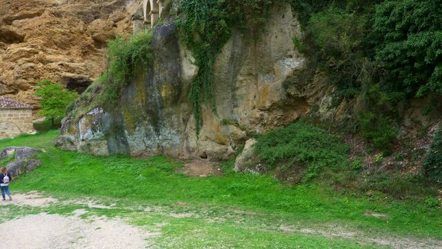 Tourist woman strolling next to the medieval church located next to the rock cliff, Tobera, Burgos.