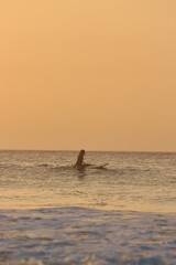 man sitting in a surfboard in the middle of the sea during the sunset