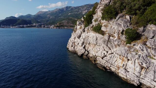 Aerial view of drone moves along beautiful nature landscape coastline of blue water sea and cliffs with typical Adriatic vegetation. Montenegro, near Milocer and Queens beach, Sveti Stefan