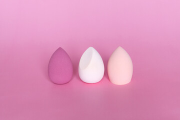Three colorful beauty blenders or makeup sponges on pink background. Cosmetic tool concept.