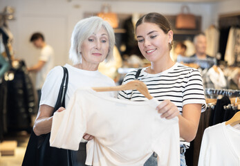 After inspection of stores assortment, customers chooses jemper on hangers and closely examine its details, feels texture of fabric. Young girl consults senior female friend about quality item