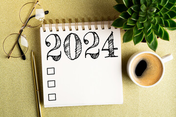 2024 New year resolutions on desk. 2024 goals list with notebook, coffee cup, plant on golden...