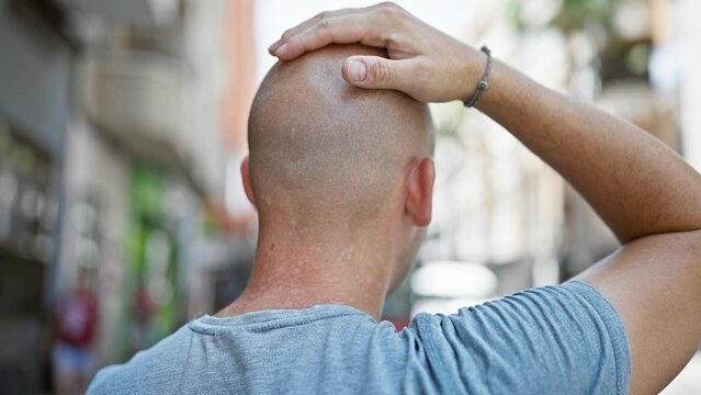 Young hispanic man standing backwards touching head at street