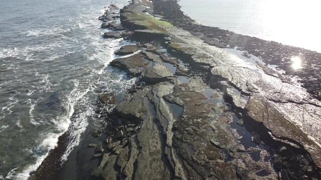 Drone shot of North Sea waves crashing on the stone pier of Filey Brigg peninsula, Filey, England