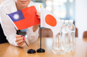 Female hands placing flags of Chinese Republic of Taiwan and Japan on table before international...