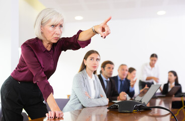Portrait of furious mature senior white female executive manager standing with outstretched hand directed towards the door thus forcing her subordinate employee out during a meeting in conference room - obrazy, fototapety, plakaty