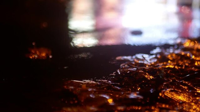 A puddle on the road with autumn leaves during the rain. Close-up shooting at night, the reflection of headlights is visible in the water.
