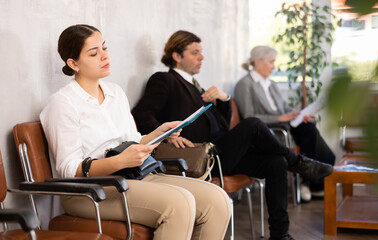 Young confident woman is sitting in the lobby of a large company, waiting for her turn to see a...