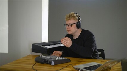 A young Caucasian musician composes a song in a music studio. Focused young man in headphones with a synthesizer. A young composer in headphones composes music.