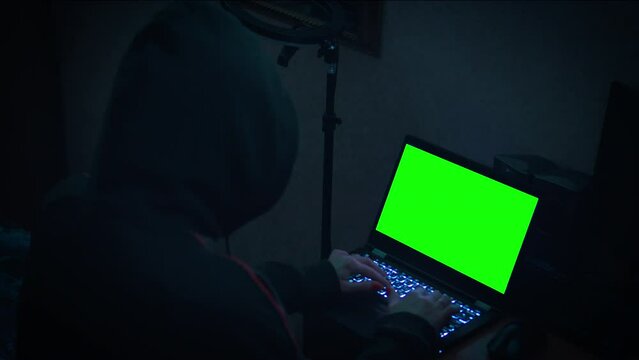 Female hacker sits in dark room in hood in front of laptop screen. Cybersecurity concept.