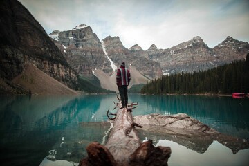 a person on a log at a lake looking out over a large lake and mountain