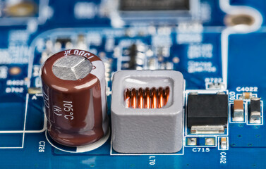 Closeup of inductor, electrolytic capacitor or transistor on blurry PCB background. Blue power...