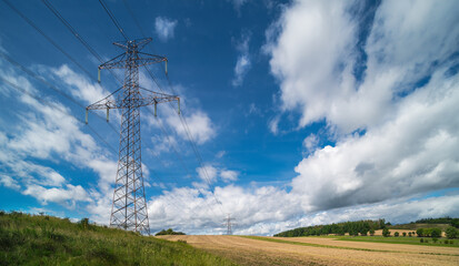 Overhead power line pylon in summer landscape with blue sky and puffy white clouds. Electric truss...