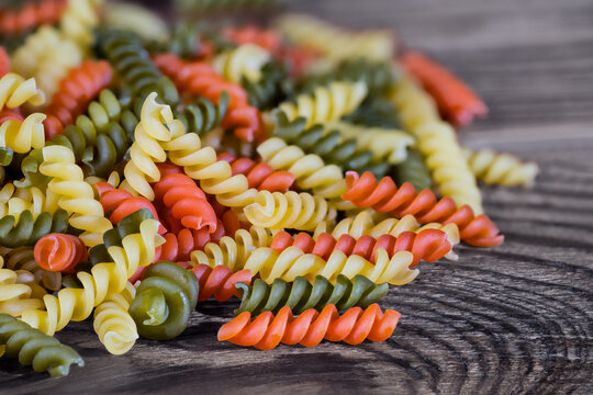 Heap of yellow, red and green fusilli pasta of helical shape on brown wooden background. Close-up a pile of raw colored egg rotini of tomato or spinach flavor. Staple food for Italian cuisine cooking.