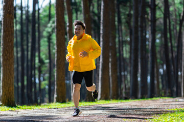 Asian trail runner is running outdoor in the pine forest dirt road for exercise and workout...