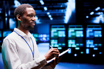 Experienced IT admin evaluating server rigs using renewable sources to reduce electronics carbon footprint. Engineer checking contingency plan on clipboard in sustainable high tech facility