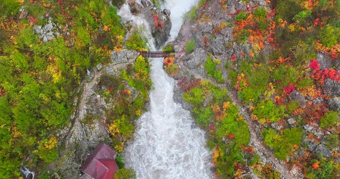 A man crossing a bridge over a river overfilled with water from the extreme weather of Autumn in Thethi national park, Albania. 