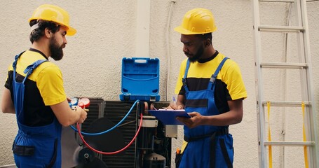 Expert technicians team working with manifold gauges to check air conditioner refrigerant levels, writing result on clipboard. Skillful mechanics using barometer benchmarking hvac system tool - obrazy, fototapety, plakaty