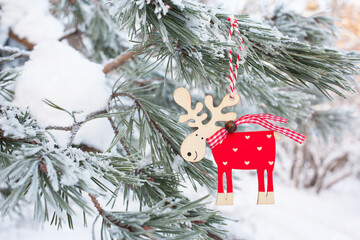 Pine branches in snow and frost, decor of a toy deer in a red sweater. Winter Christmas card.