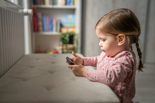 Naklejki One girl toddler child play video game on mobile phone smartphone