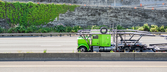 Bright green classic bonnet big rig car hauler semi truck tractor transporting empty semi trailer...