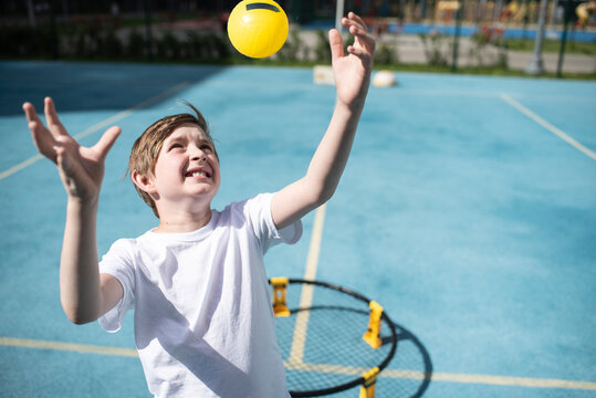 child playing sports game spikeball, spikeball. the boy is hitting the yellow ball in a miniature volleyball analog outside.