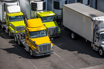 Day cab powerful big rig semi trucks with refrigerator semi trailers standing on the warehouse...