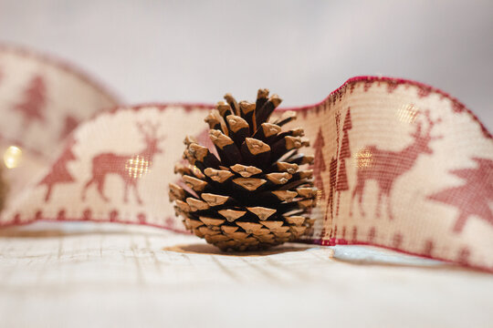 Pine cone wrapped in a festive ribbon with reindeer and tree designs and fairy lights