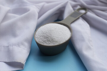 Detergent powder in measuring spoon with shirt before washing. Laundry concept.