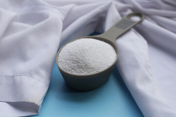 Detergent powder in measuring spoon with shirt before washing. Laundry concept.